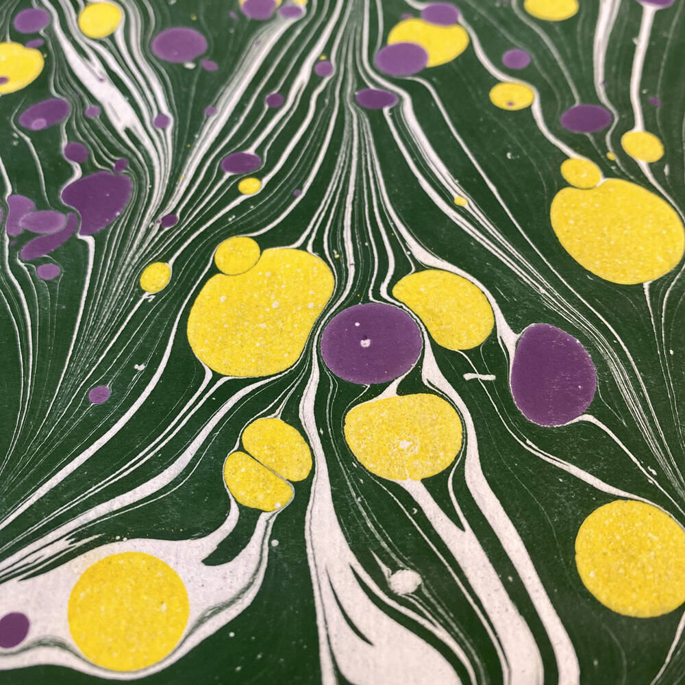 Marmorpapier / marbled paper in den Farben grün, gelb und violett. Das Muster ist durchzogen mit Flecken.
